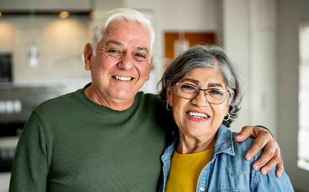 A couple, representing a 65+ ALICE household, smile at the camera in their home with their arm around each other.